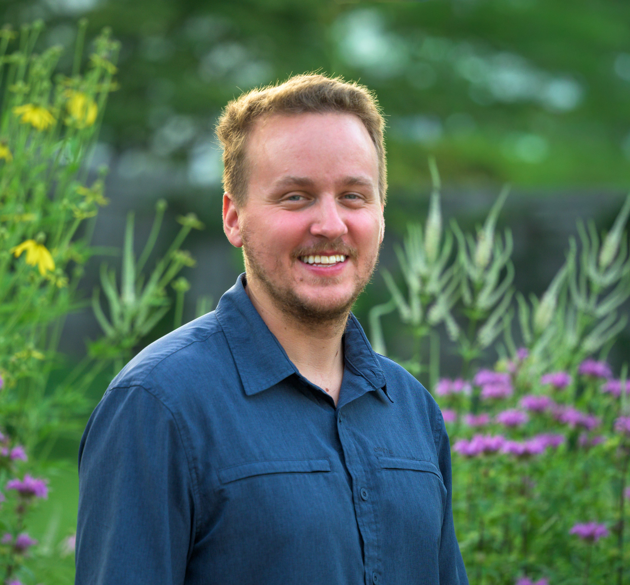 Todd Testerman, owner of Edaphic Garden Consulting, smiling in a native garden with bee balm and Culver's root behind him